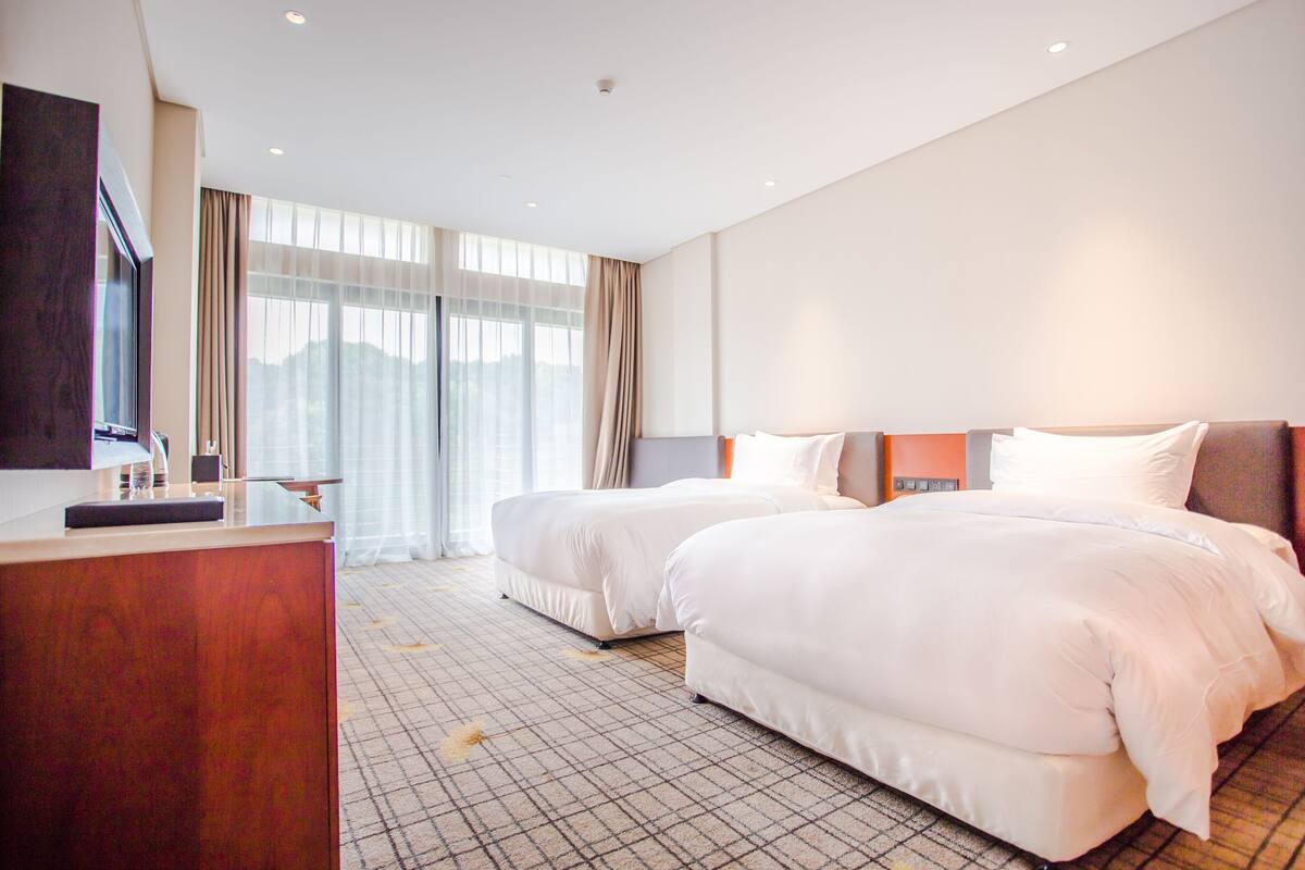A hotel room with two beds, a desk, and a large window with curtains.