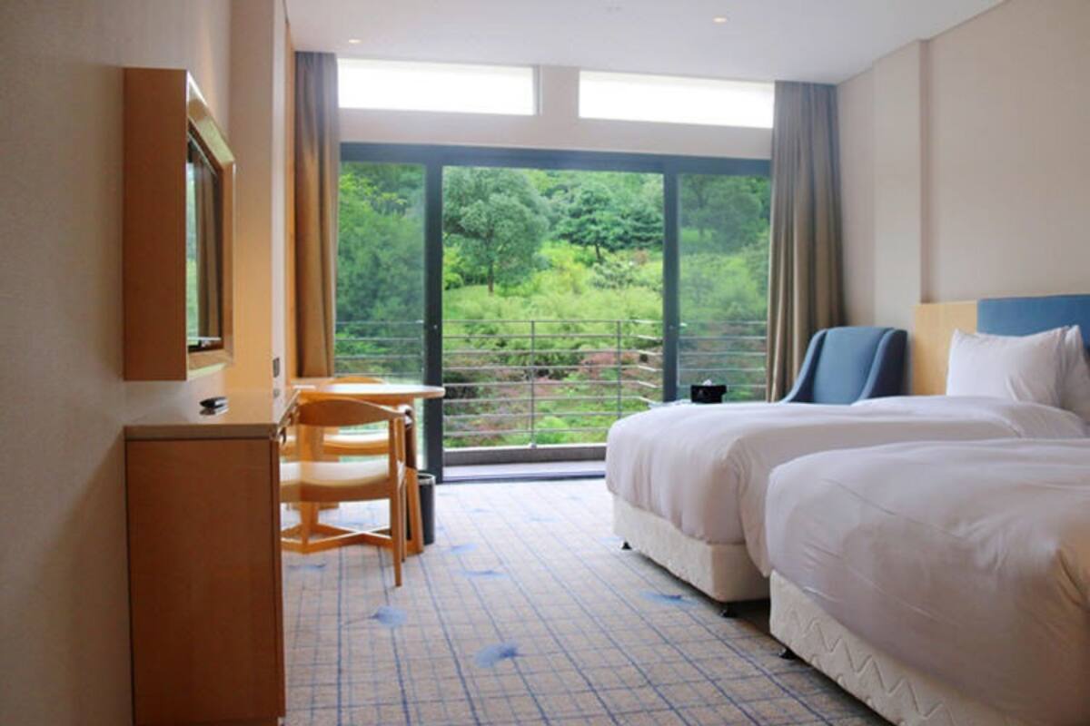 A hotel room with a large window, a desk, two beds, and a wardrobe.