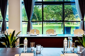 A conference room with a large window overlooking a grassy area. There are several chairs and tables set up with water bottles and glasses.
