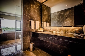 A modern bathroom with a large mirror, marble countertops, and a glass-enclosed shower area.