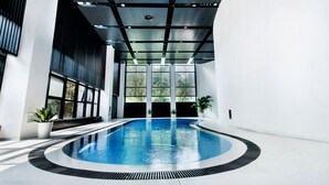 An indoor swimming pool with a modern design, surrounded by large windows and potted plants. - Preess Resort Hotel (Changsha)
