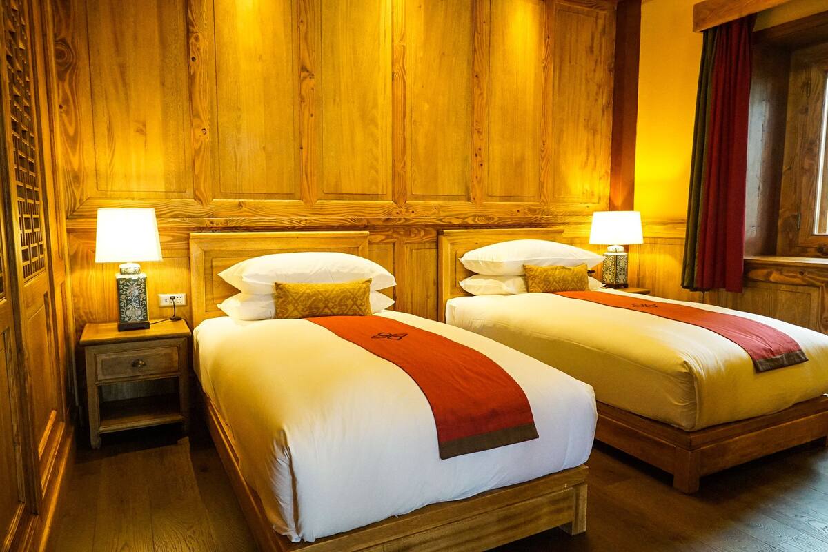 A hotel room with two beds, wooden paneling, nightstands with lamps, and a window with curtains.