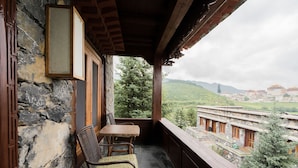 A balcony with a wooden table and chairs, stone walls, and a view of a monastery in the distance. - Songtsam Linka Shangri-La (Deqin)