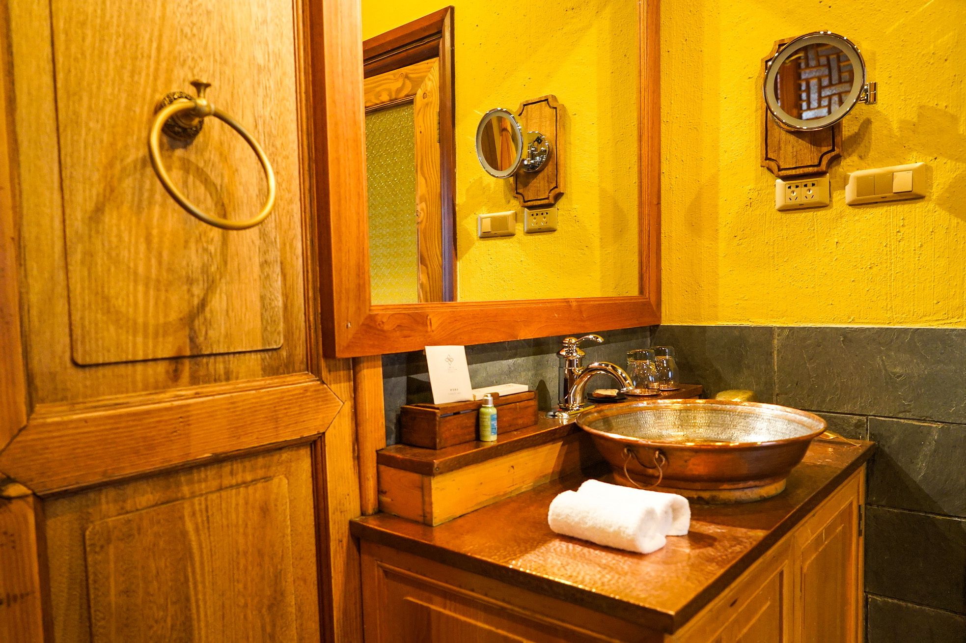 A wooden vanity with a copper sink, a mirror, and a towel.