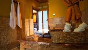 A bathroom with a stone wall, a wooden bench, a wicker basket, and towels hanging on a rack. - Songtsam Linka Shangri-La (Deqin)