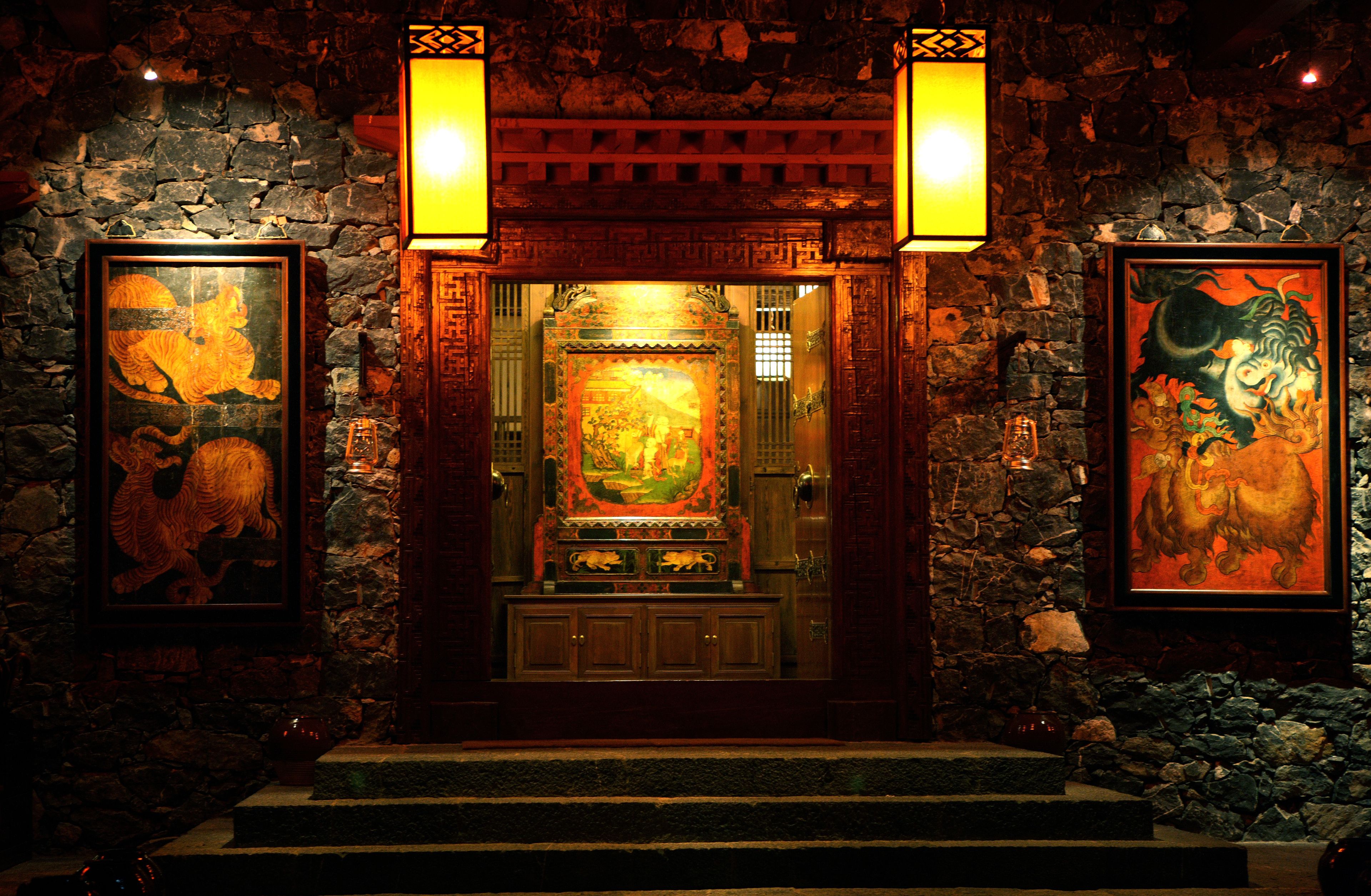 A traditional interior with stone walls, a wooden altar, and two illuminated lanterns.