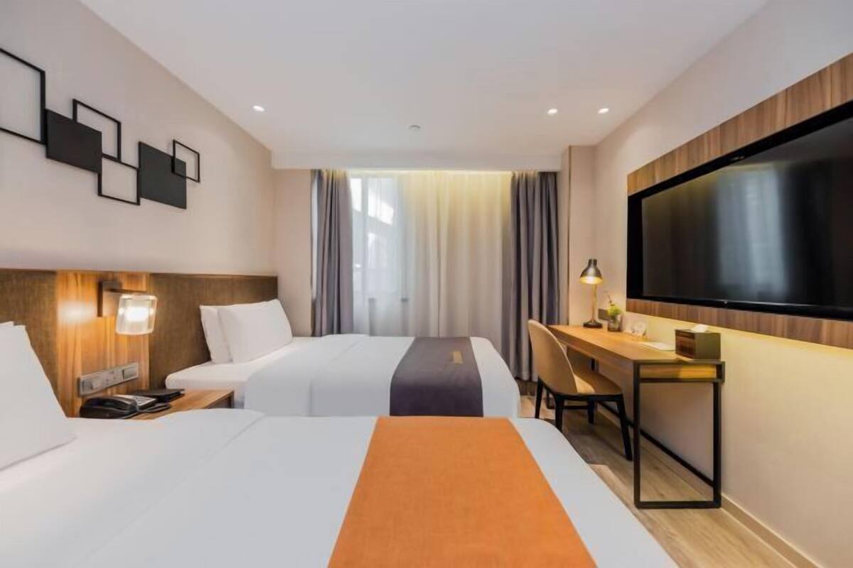 A hotel room with two beds, a desk, a TV, and a wall-mounted artwork.