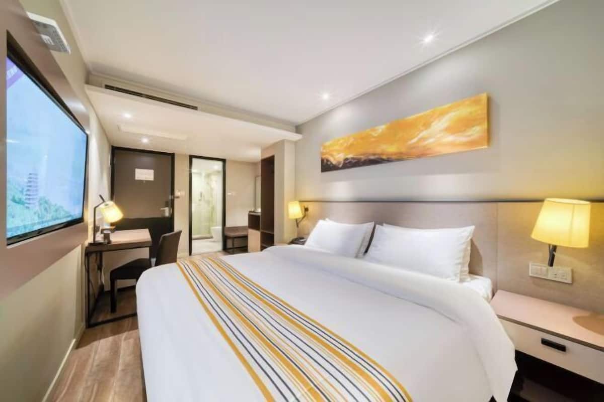 A hotel room with a large bed, a desk with a chair, a TV, and a painting on the wall.