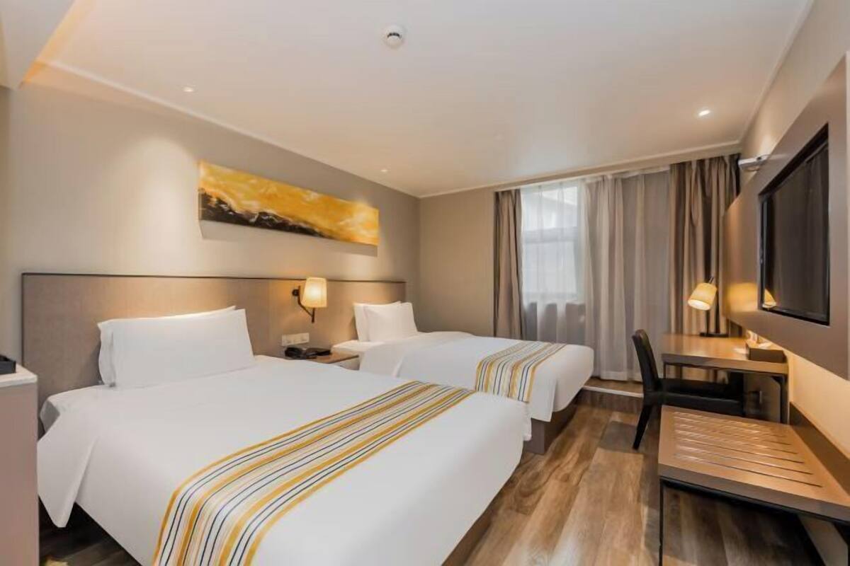 A hotel room with two beds, a desk, a chair, a TV, and a painting on the wall.