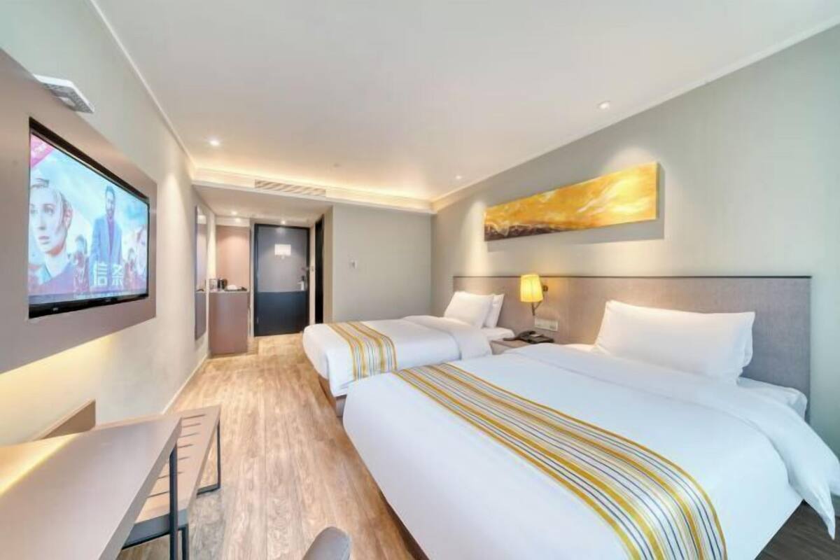 A hotel room with two beds, a TV mounted on the wall, a desk, and a wooden floor.