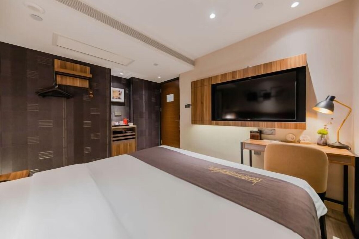 Moderni hotellihuone, jossa on suuri sänky, työpöytä, taulutelevisio ja pieni keittokomero.