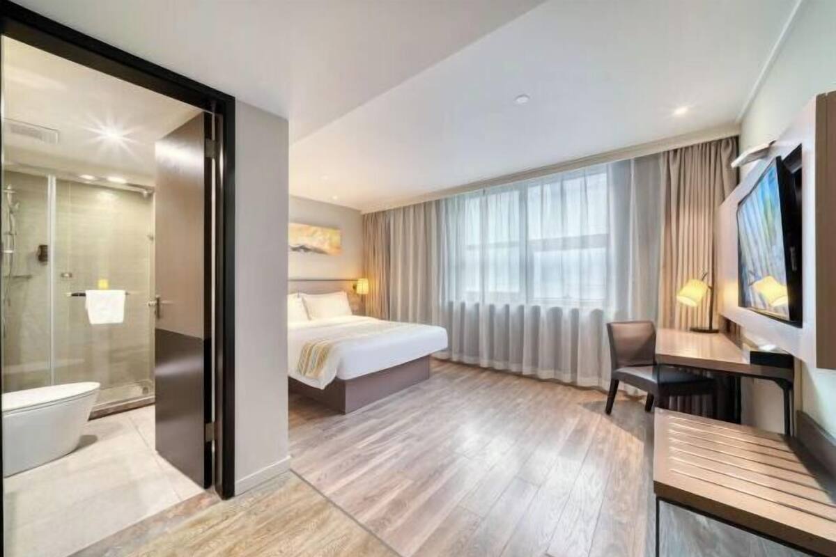 A modern hotel room with a bed, a desk, a TV, and a shower area.
