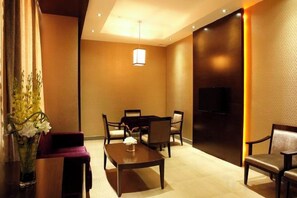 Une chambre d’hôtel équipée d’une table à manger, de chaises, d’un canapé, d’une télévision et d’un vase avec des fleurs.