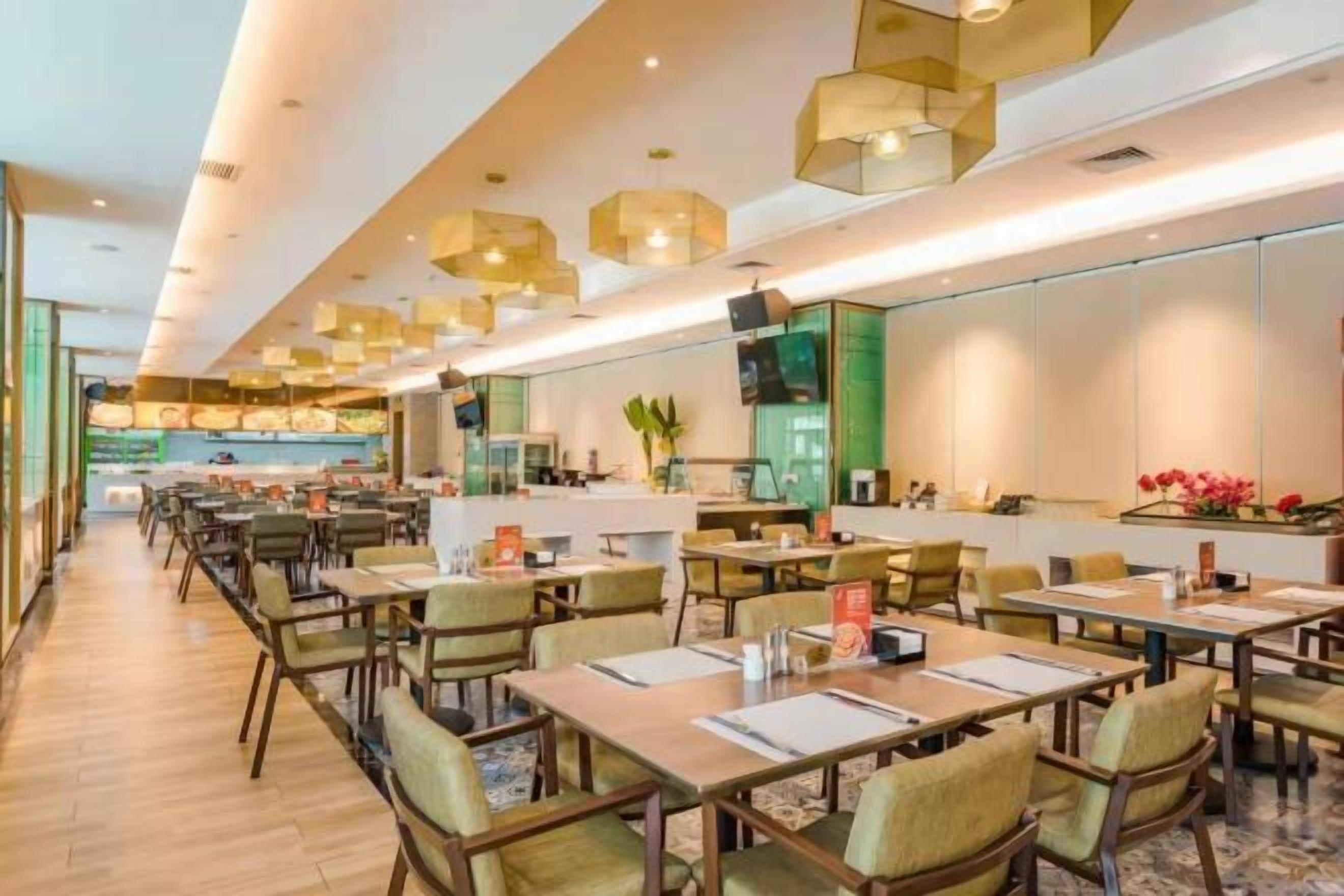 A modern restaurant with multiple dining tables and chairs, a kitchen area in the background, and pendant lighting.