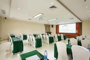 Une salle de conférence avec des rangées de tables, de chaises et un écran de projection.