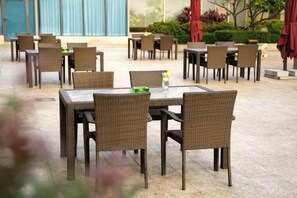 Un espace de restauration en plein air avec des tables et des chaises en osier, dont certaines sont agrémentées de sets de table verts.