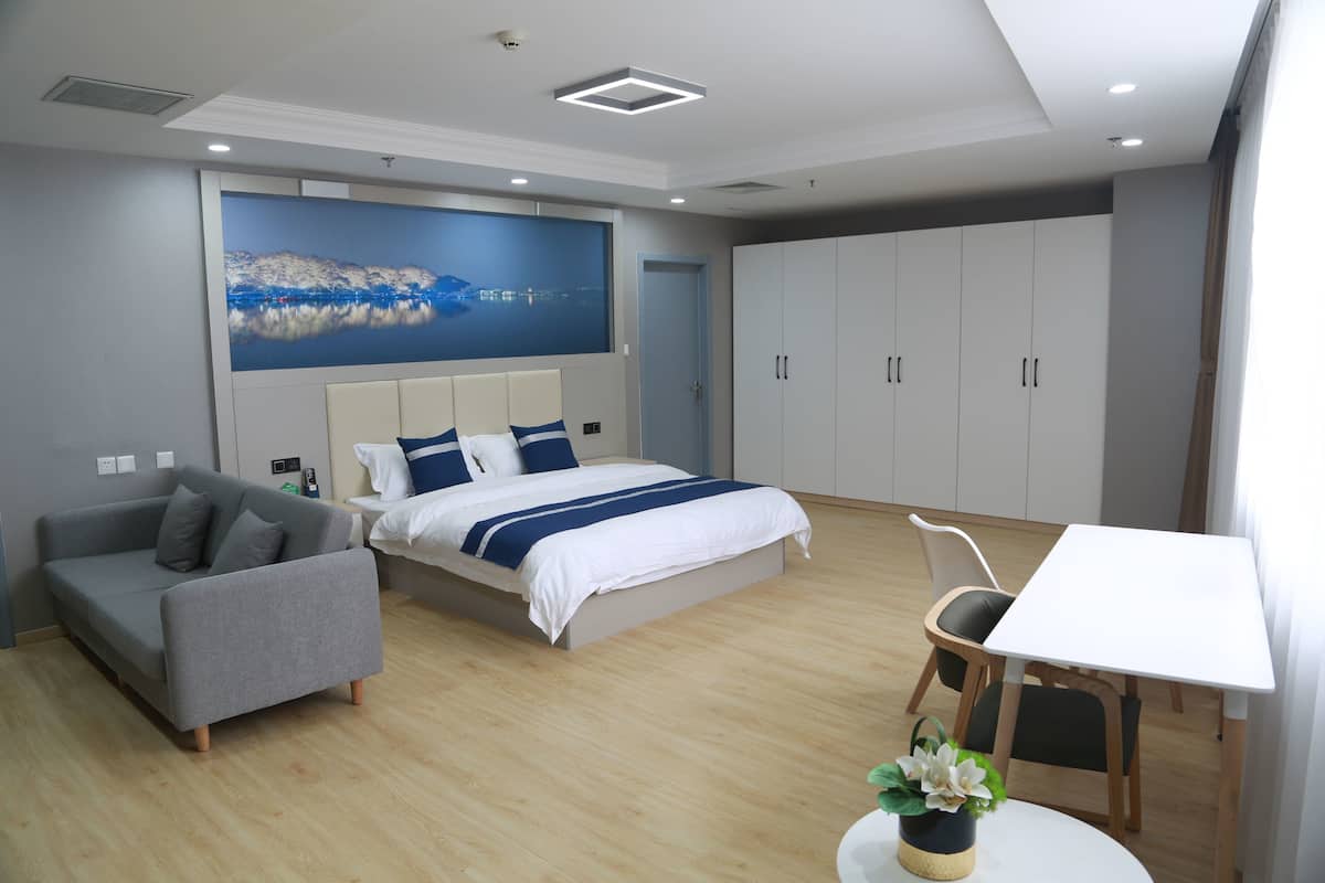 A modern bedroom with a bed, a sofa, a dining table, and a large wardrobe.