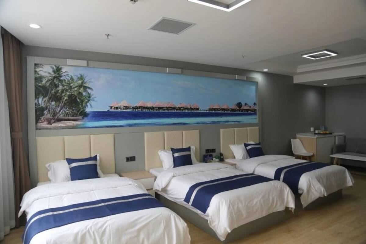 A hotel room with three beds, a desk, and a large painting of a beach scene.