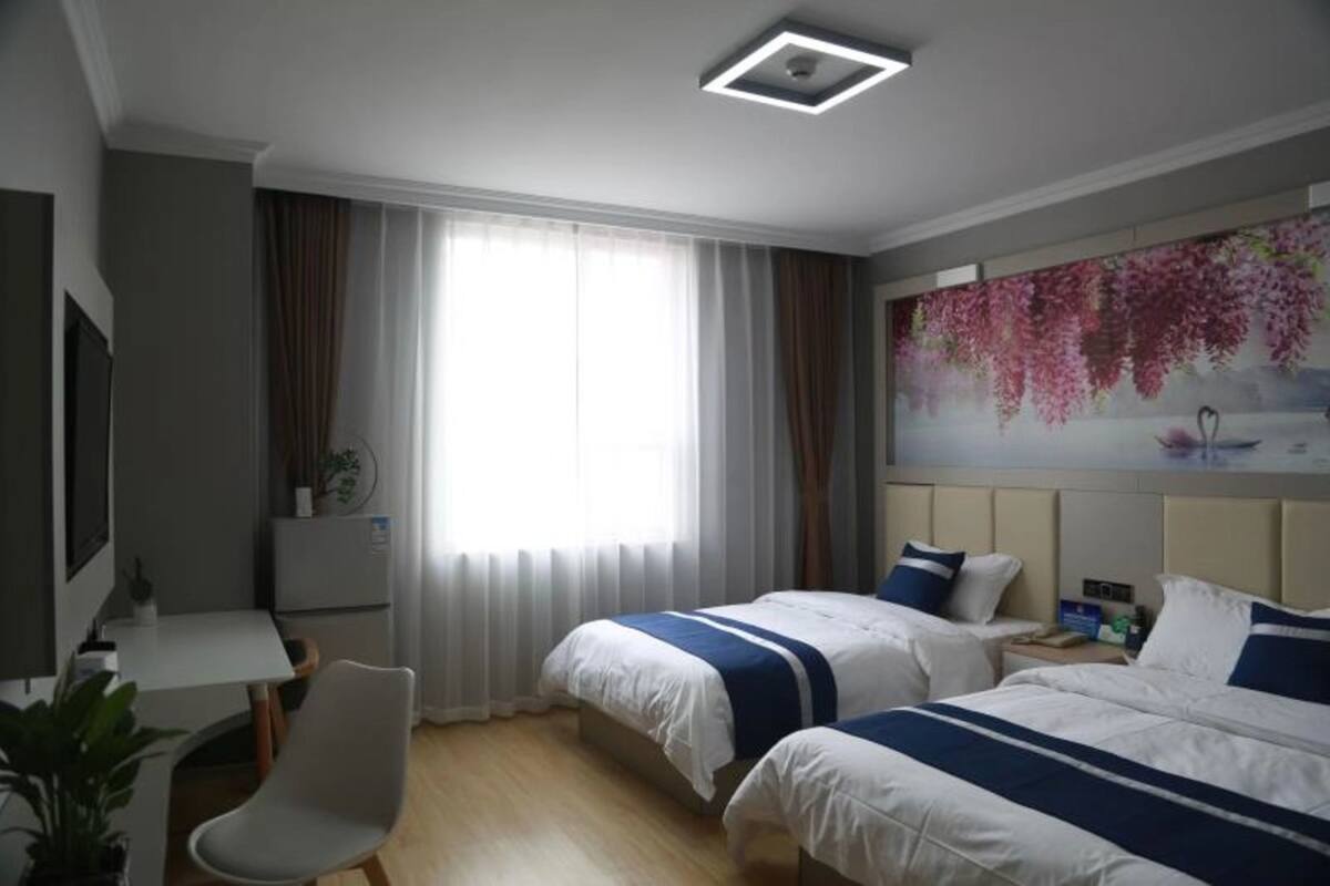 A hotel room with two beds, a desk, a chair, a TV, and a large window with curtains.