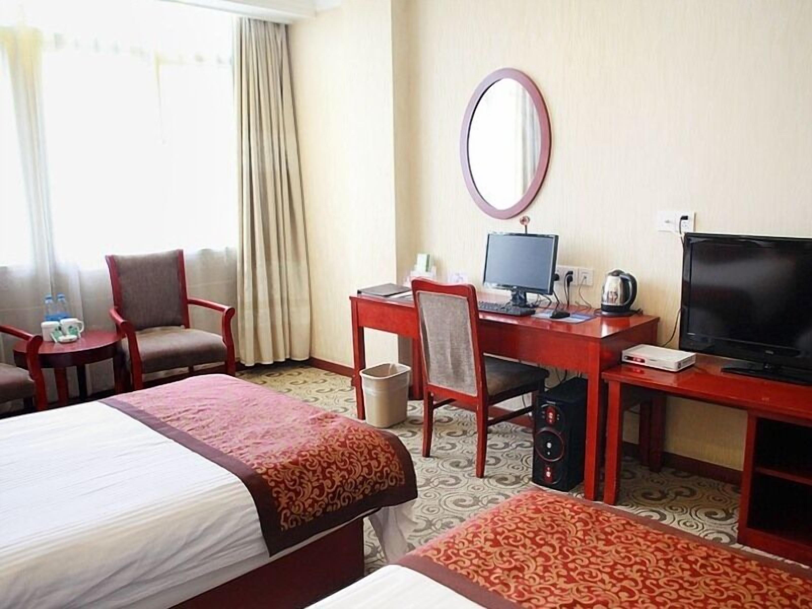 Habitación de hotel con dos camas, un escritorio con computadora, televisor y una silla.