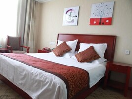 Habitación de hotel con una cama grande, dos almohadas, una mesita de noche, una silla y una obra de arte en la pared.