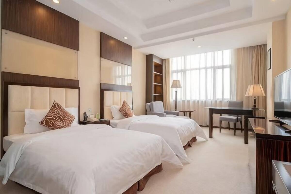 Ein Hotelzimmer mit zwei Betten, einem Schreibtisch, einem Sessel, einem Fernseher und einem großen Fenster.