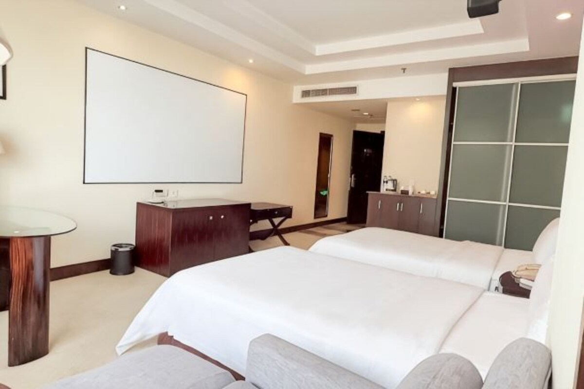 A hotel room with a large bed, a desk, a chair, a TV, and a wardrobe.