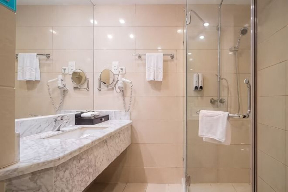 A bathroom with a marble sink, two mirrors, a shower, and a glass-enclosed shower area.