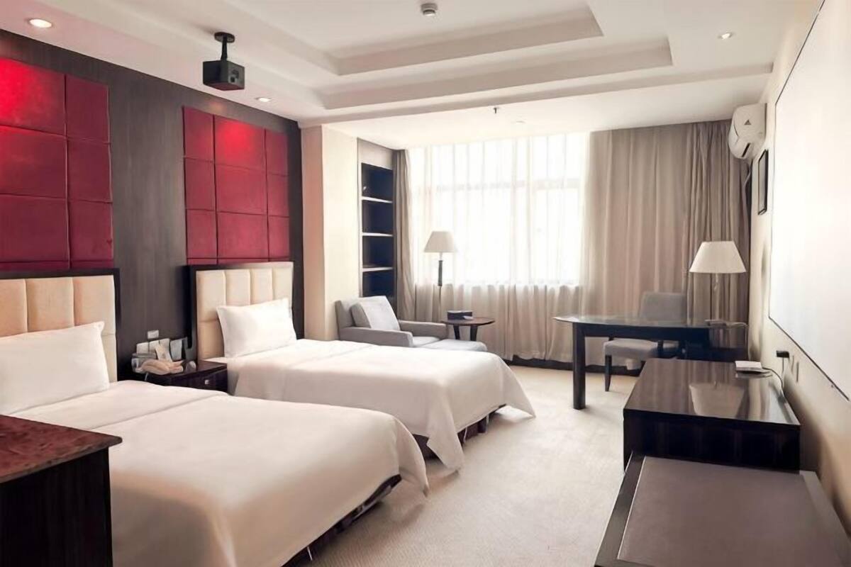 Ein Hotelzimmer mit zwei Betten, einem Schreibtisch, einem Sessel, einem Fernseher und einem großen Fenster mit Vorhängen.