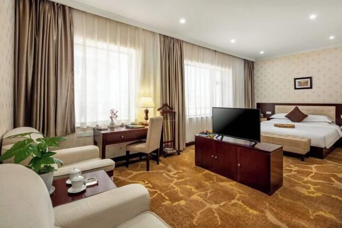A hotel room with a bed, a desk with a chair, a television, and a coffee table.