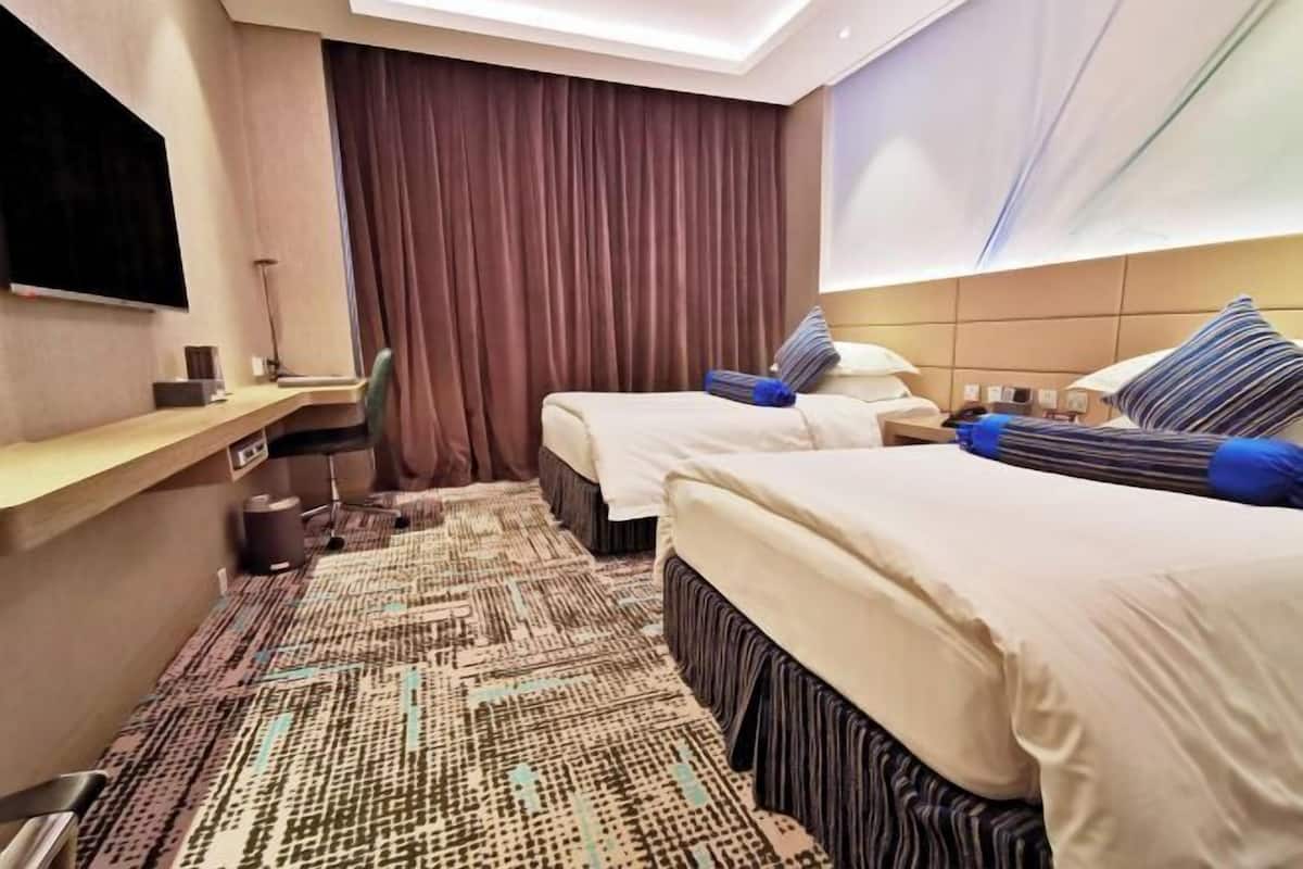 Een hotelkamer met twee bedden, een bureau, een stoel, een televisie en een groot raam met gordijnen.