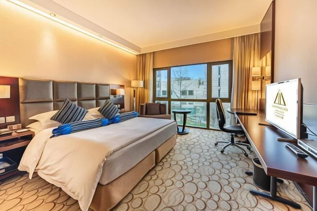 Een hotelkamer met een groot bed, een bureau met een computer, een televisie en een raam met uitzicht op gebouwen.