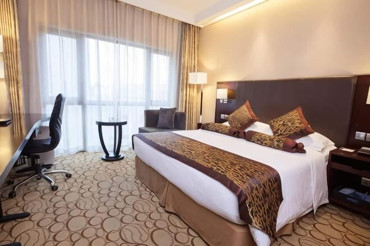 Een hotelkamer met een groot bed, een bureau, een stoel, een klein tafeltje en een nachtkastje.