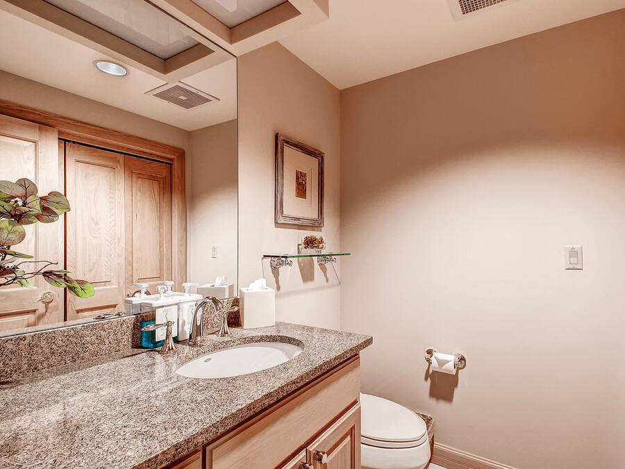 Un baño con encimera de granito, un lavabo blanco, un espejo y un inodoro.