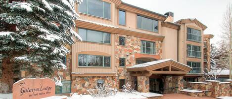 A multi-story lodge with a stone facade, a snow-covered entrance, and a sign indicating the name and address.