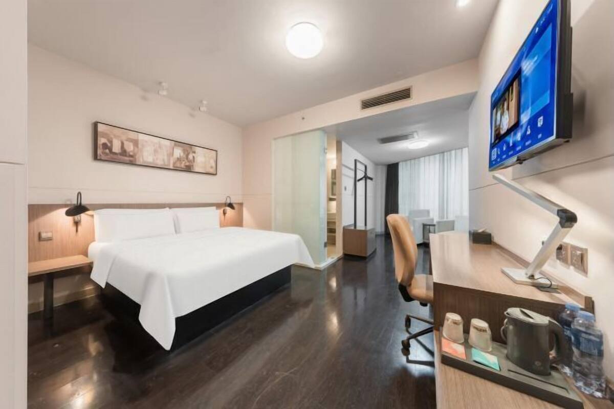 Una habitación de hotel moderna con una cama grande, un escritorio con computadora, un televisor de pantalla plana y un cuadro en la pared.