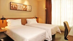 Een hotelkamer met twee bedden, een nachtkastje met telefoon, een ingelijste foto aan de muur en een raam met gordijnen.