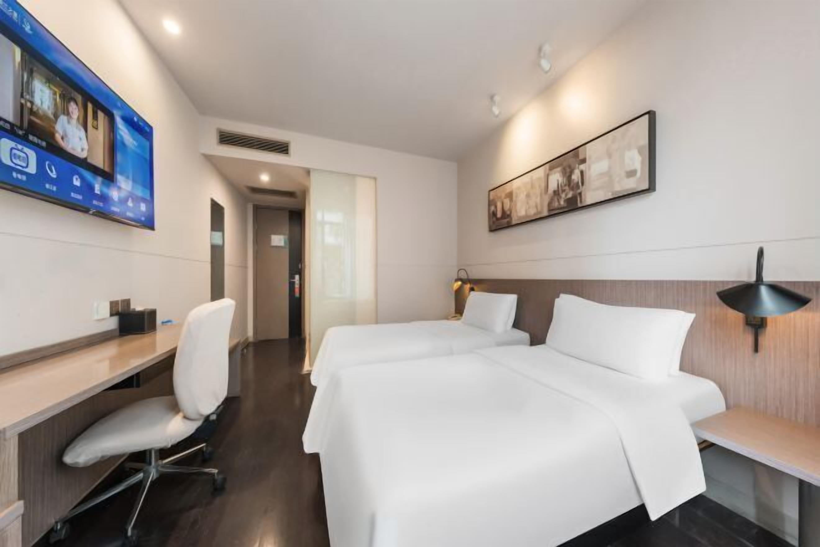 Hotellihuoneessa on työpöytä, kaksi sänkyä, televisio ja seinällä oleva kehystetty taulu.