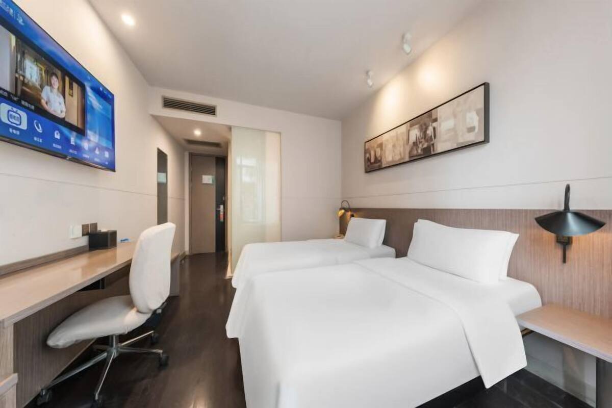 Una habitación de hotel con escritorio, dos camas, televisión y un cuadro en la pared.