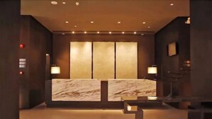Een receptiehal met een marmeren receptiebalie, een ruime wand met verticale panelen en een kleine tafel met een lamp.