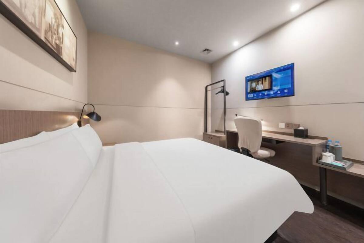Habitación de hotel con cama, escritorio, silla, televisor montado en la pared y zona de ducha.