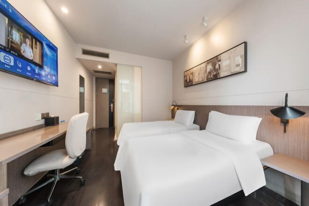 Een hotelkamer met een bureau, twee bedden, een televisie en een ingelijst kunstwerk aan de muur.