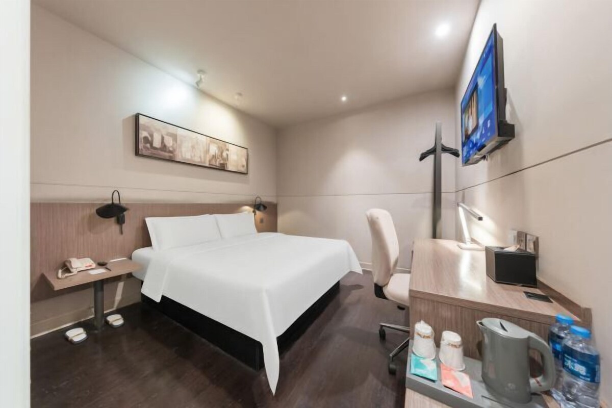 Une chambre d’hôtel équipée d’un lit, d’une table de chevet, d’une chaise, d’un bureau, d’une télévision et d’une œuvre d’art accrochée au mur.
