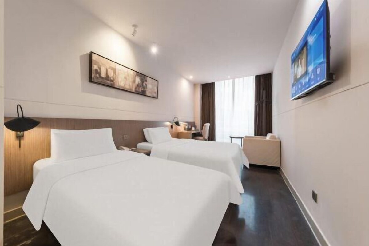 A hotel room with two beds, a desk, a chair, a TV, and a painting on the wall.