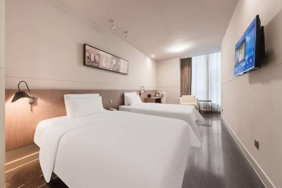 Habitación de hotel con dos camas, un escritorio, una silla, un televisor de pantalla plana montado en la pared y un cuadro sobre la cama.