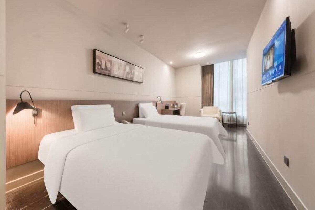 Een hotelkamer met twee bedden, een bureau, een stoel, een flatscreen televisie die aan de muur is bevestigd, en een schilderij boven het bed.