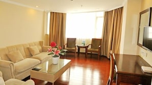 Habitación de hotel con sofá, mesa de centro de vidrio, televisor, pequeña mesa de comedor y una silla.