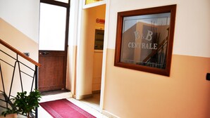 A hallway with a wooden door, a potted plant, and a red carpet leading to a room with a sign reading "B&B CENTRAL". - B&B Centrale (Reggio Calabria)