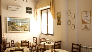A dining area with round tables, chairs, and a painting on the wall. - B&B Centrale (Reggio Calabria)