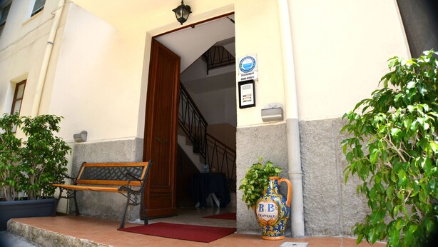 A building entrance with a wooden bench, a potted plant, and a sign. - B&B Centrale (Reggio Calabria)